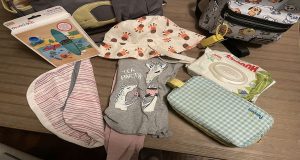 Diapers, wipes, clothes, placemats, hat, and wet bag waiting to be put in a diaper bag