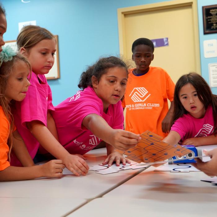 group-of-kids-from-boys-and-girls-club-of-america-standing-around-table-figuring-out-a-puzzle