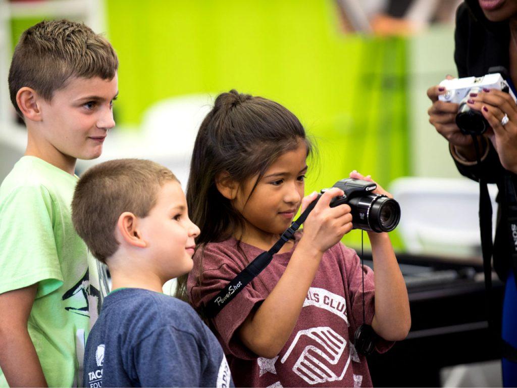 kids-from-boys-and-girls-club-of-america-two-boys-standing-and-girl-holding-camera-in-room-looking