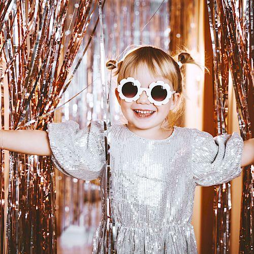 family-friendly new years eve events Happy little stylish girl in shiny dress having fun. Festive background with foil curtain decorations for kids birthday or fancy dress party, disco music or New Year. Celebration and Holiday concept.